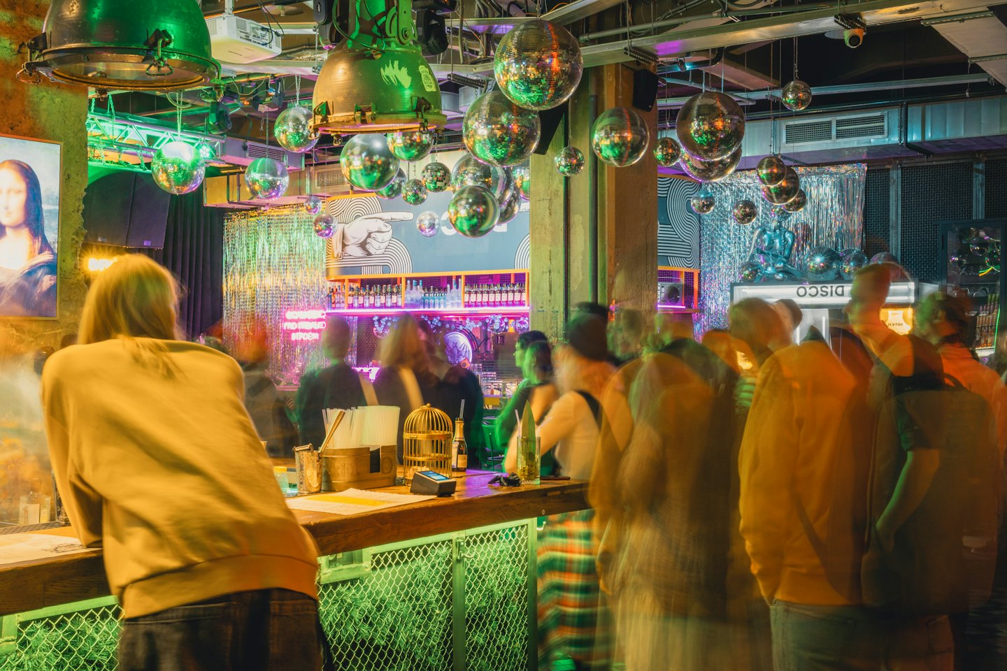 Patrons mingle at a bar decorated with disco balls and neon.
