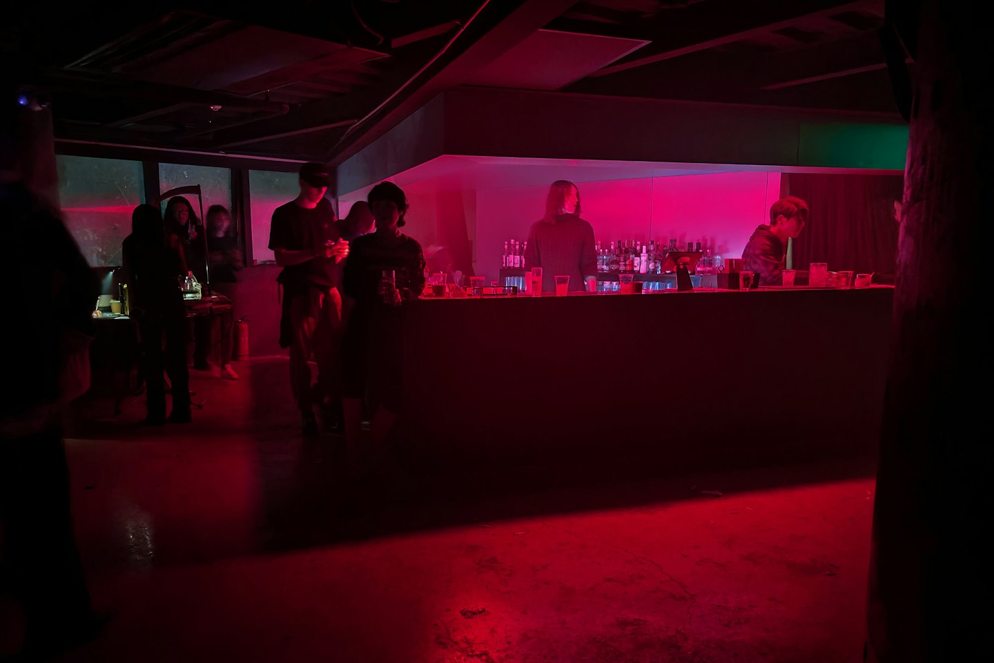Patrons socialize with a bartender at a modern neon bar.