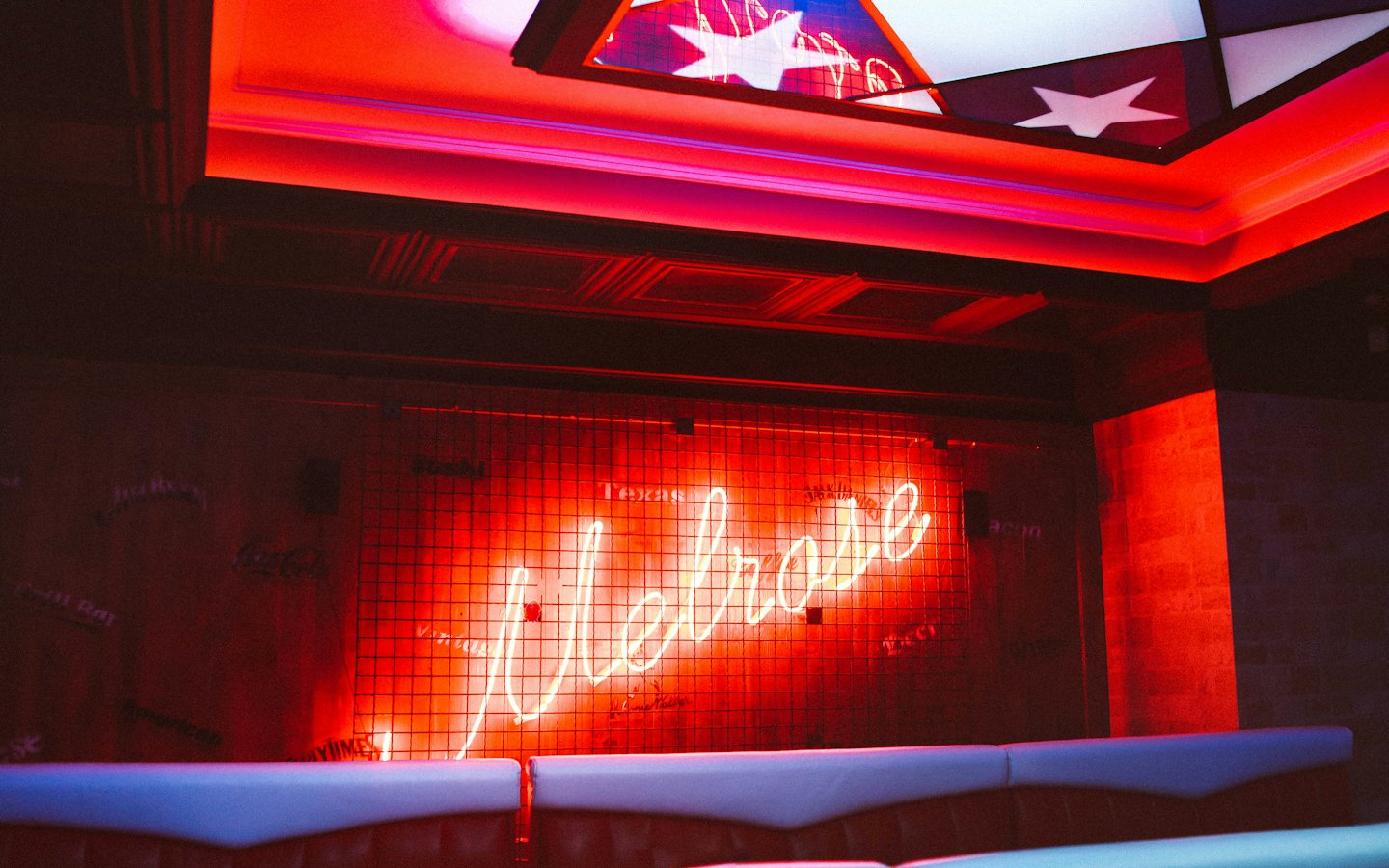 Neon "Melrose" sign glowing in a dark bar setting.