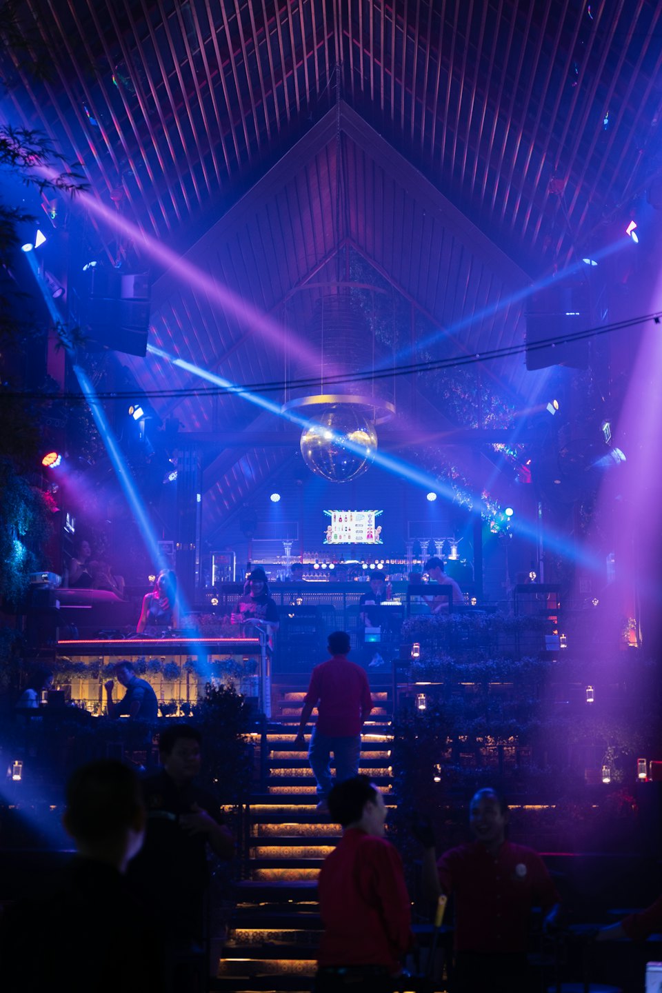 Crowd gathers in a multi-level nightclub as a DJ performs.