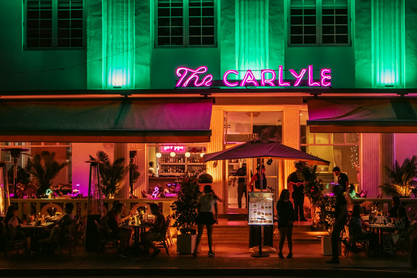 Patrons dine on an outdoor patio at a neon-lit restaurant.